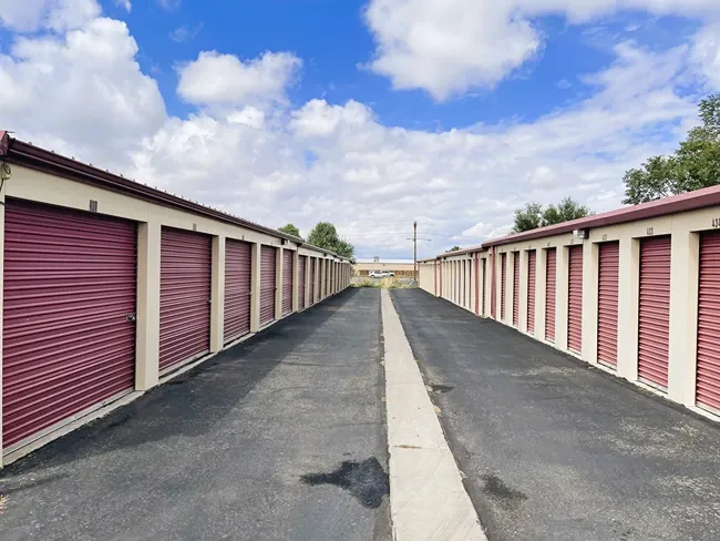 Outdoor storage units with wide paved aisle at Alice's Attic Self Storage facility.