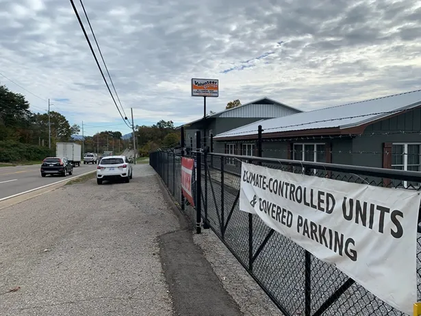 Front view of fenced in Volunteer Storage Maryville 2 storage facility. Banner on fence says "Climate-controlled units &...