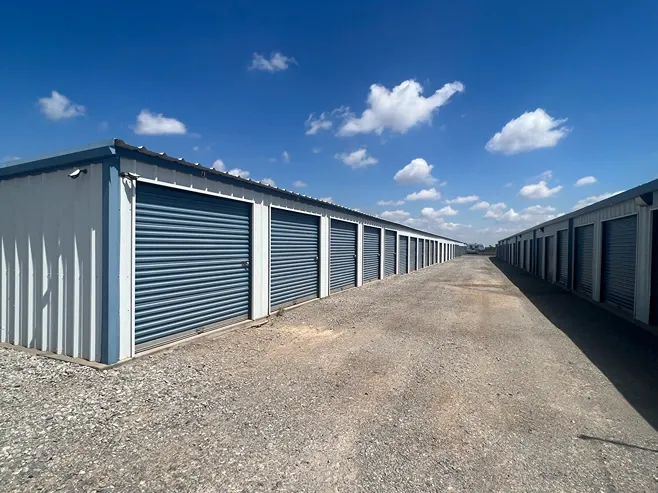 Drive-up storage units with roll-up doors and wide gravel access lanes at Texoma Self Storage.