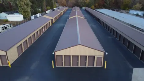 Storage buildings with gravel access and tree-lined backdrop at Lambertville Mini Storage Secor.