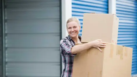 White woman smiling and carrying boxes to a storage unit