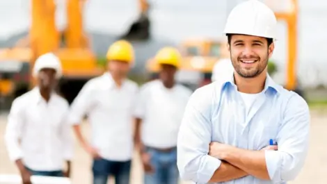 Male contractor with arms crossed in the foreground, 3 men in helmets in the background